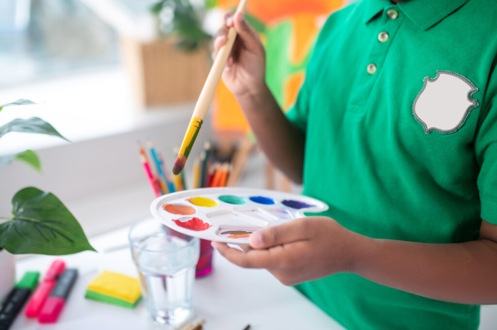 Boys hands holding paintbrush over palette with paints